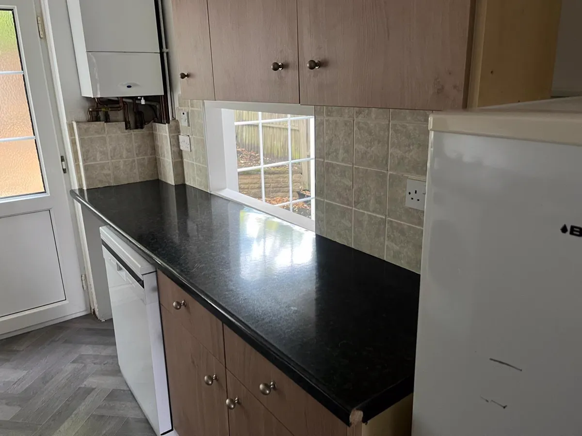 Clean kitchen with black worktop, wood cupboards and dishwasher