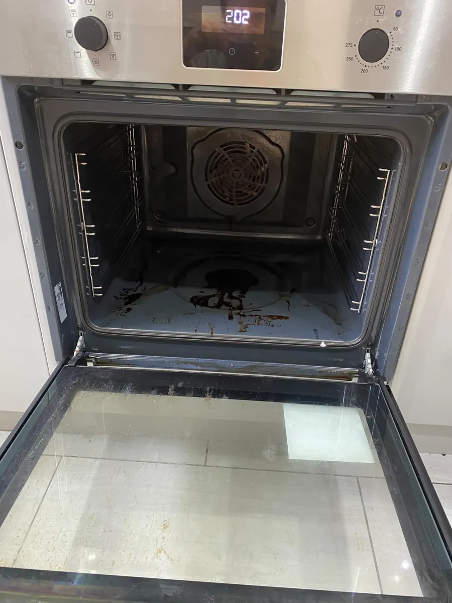 Built-in oven with burnt-on grease on the floor and a smeared door glass before cleaning